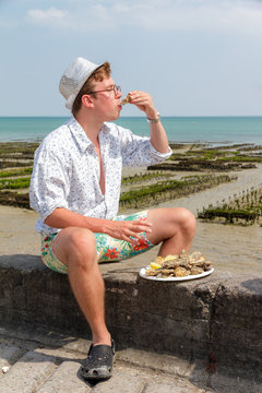 Young man enjoys the taste of fresh raw oysters at the french coast of Brittany (Bretagne) in Cancale, France on a summer day