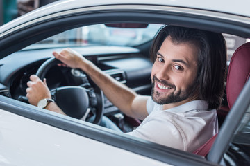 smiling bearded man sitting in new car for test drive in dealership salon