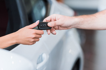 Obraz na płótnie Canvas cropped shot of man giving car key to woman at dealership salon