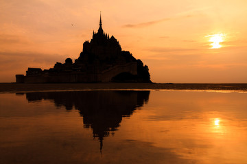 Fototapeta premium Beautiful view of historic landmark Le Mont Saint-Michel in Normandy, France, a famous UNESCO world heritage site and tourist attraction, at sunset with reflection