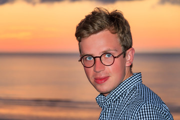 Fototapeta premium Beautiful portrait of a young caucasian man at sunset at the beach looking at the camera