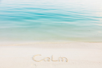 The Word Calm Written in the Sand on a Beach with blue sea background