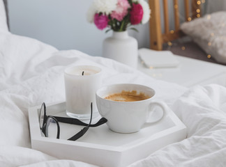 Fototapeta na wymiar Coffee, candle and glasses on the tray standing on the bed.