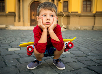 A little boy with a skateboard in his arms rests and thinks