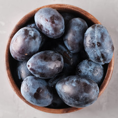 Plums. Fresh ripe washed plums in a wooden bowl close-up on a neutral background.