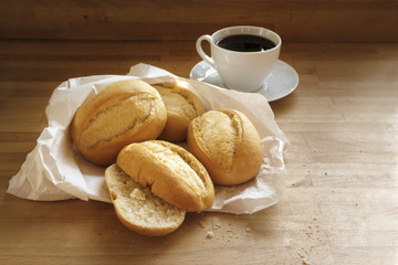 bread rolls or buns in a white paper bag and a cup of coffee on a wooden table, copy space