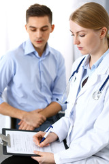 Female doctor holding application form while consulting man patient in hospital office. Medicine and healthcare concept