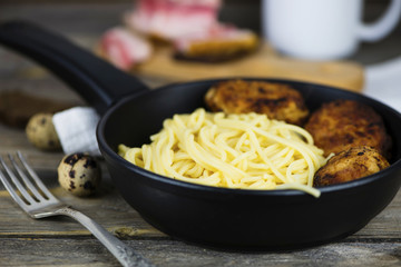 Spaghetti with meat cutlets in a frying pan on a wooden board