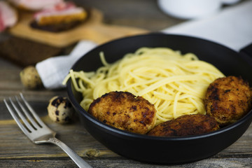 Spaghetti with meat cutlets in a frying pan on a wooden board