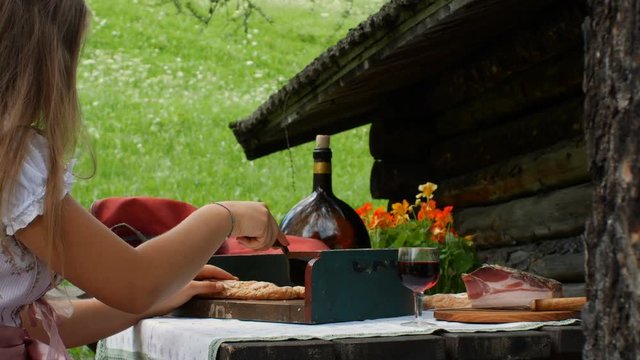 a teenager dressed in a typical Tyrolean dress cuts dry bread with a typical Tyrolean bread cut