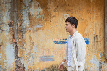 Obraz na płótnie Canvas Asian man in casual clothes standing on old wall background.