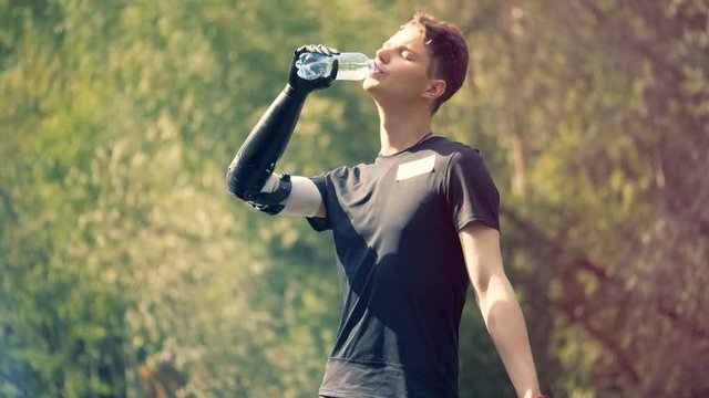 Teenager is holding a bottle with his prosthetic hand and drinking from it outdoors