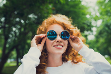 beautiful red-haired girl in sunglasses walking in the Park