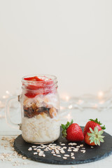 Homemade overnight oats with fresh strawberry served in a  a tall glass jar on black slate board. Healthy breakfast