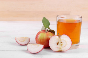 Apple juice in a glass with mature fresh red apples on a white wooden table
