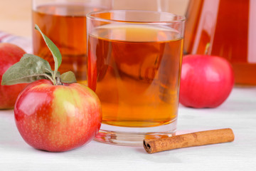 Apple juice in a glass with mature fresh red apples and cinnamon on a white wooden table