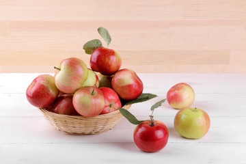 Fresh ripe red apples with leaves in a basket on a white wooden table and on a background of natural wood