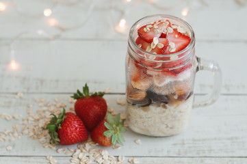 Overnight oats with fresh strawberry and whole grain cereal served in a tall glass jar on wooden table