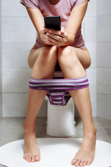 Woman using smartphone while sitting in toilet