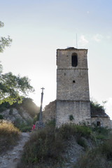 Fototapeta na wymiar The Iglesia de San Miguel church calvary and the bell tower covered with climbing ivy in Janovas, a ruined village in the Aragonese Pyrenees abandoned during the sixties due to the building of a dam