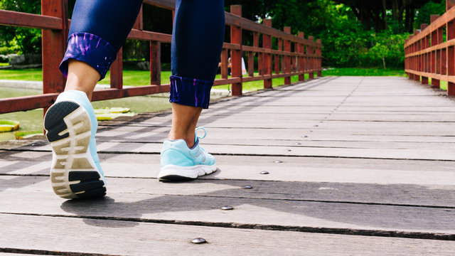 Sporty women walking on the wooden bridge, Close up of feamale sport shoes walking or jogging alone at park in the morning, Sports healthy lifestyle concept.