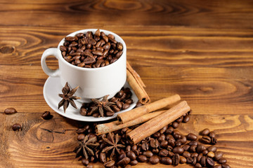 Coffee beans in white cup, cinnamon sticks and star anise on wooden table