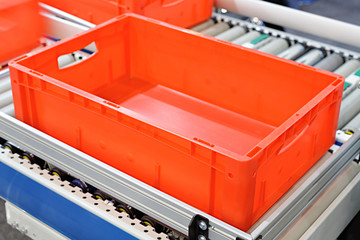 Red plastic containers on roller conveyors in an automated high bay warehouse. The boxes are used...