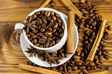 Coffee beans in white cup, cinnamon sticks and star anise on wooden table. Top  view