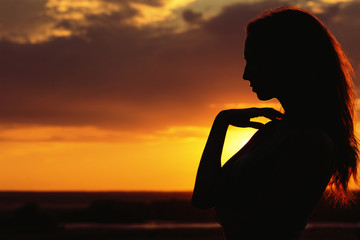 silhouette of a beautiful girl at sunset in a field, face profile of young woman on nature