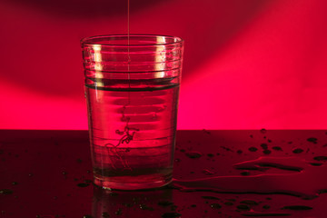 Glass of water in red background pouring honey