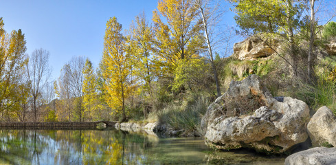 A landscape of a small pond with yellow trees, branches and rocky mountains and cliffs during autumn in the Aguallueve rural park in Anento, Aragon, Spain