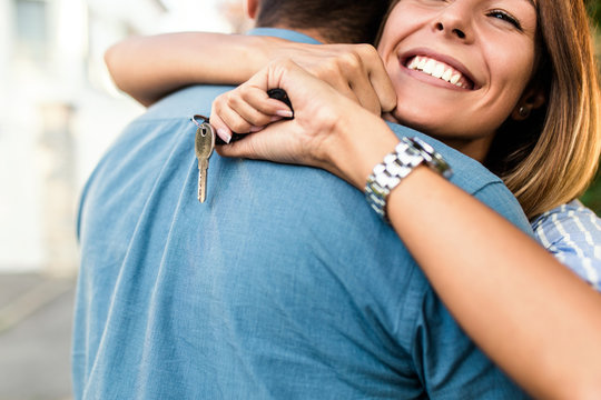 Happy Young Couple With Key In Hand Standing Outside In Front Of Their New Home.