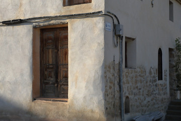 Fototapeta na wymiar A restored two sided brown door in a white and beige wall with some cables passing over it in the Almonacid de la Cuba rural country town in Aragon Region, Spain, at sunset