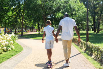 New skills. Nice caring father holding his sons hand while teaching him to ride a skateboard