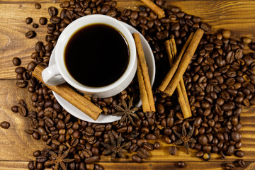 Cup of coffee, roasted coffee beans, star anise and cinnamon sticks on wooden table. Top view