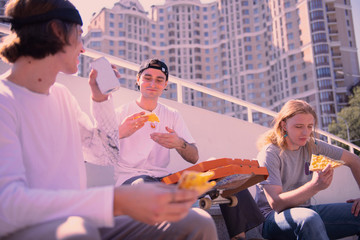 Fast food. Joyful young man drinking water while sitting in semi position on the foreground