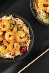 Fried prawns and rice noodles with spices on a black plate. Black background. Eastern food. Copy space. Vertical shot.
