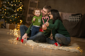 focus on caramels.A young family with a small cute baby with a caramel candy on the background of a Christmas tree and lights. Christmas, a new year, warmth and comfort of the holiday