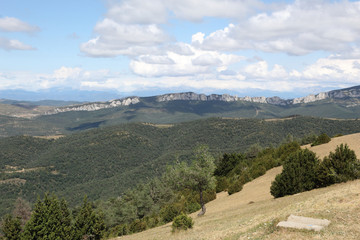 A summer landscape of the typical Pre-Pyrenees mountains from Puig Monè, with yellow grass and a blue cloudy sky in Luesi, a small town in the Aragon region, Spain