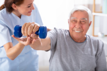 Obraz premium Nurse Helping Senior Man With Dumbbell Exercise