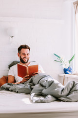 Fototapeta premium Young man reading a book in the bed