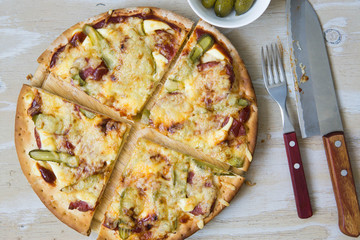 Homemade pizza with pickled cucumbers, sausages and cheese on wooden plate isolated, on white wooden background