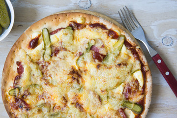 Homemade pizza with pickled cucumbers, sausages and cheese on wooden plate isolated, on white wooden background