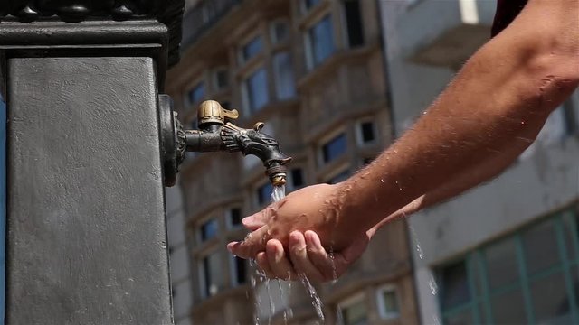Man washes his hands with water from old iron tap in the street of old city.