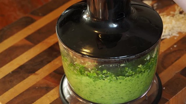 mixing grinded green basil leaves, nuts and cheese in oil