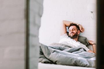 Young man waking up in the bed in the morning - obrazy, fototapety, plakaty