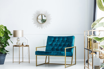 Sunburst mirror on a white wall of a fancy living room interior with golden furniture and a modern,...