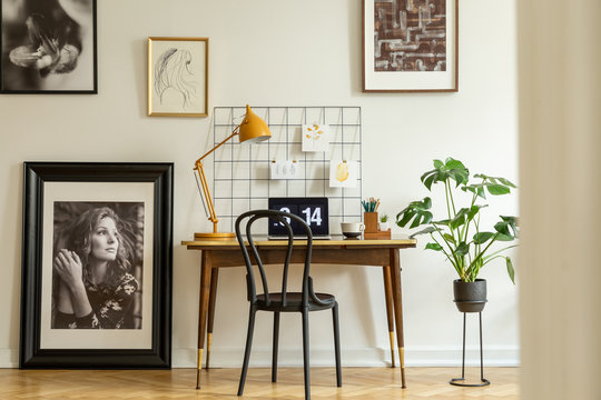 Large, framed photo and a monstera plant in a classic workspace interior with an orange lamp on a wooden desk