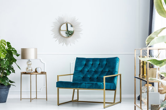 Sunburst mirror on a white wall of a fancy living room interior with golden furniture and a modern, turquoise blue sofa