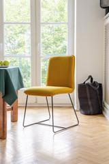 Yellow chair on a wooden floor with a balcony in the background in a dining room interior